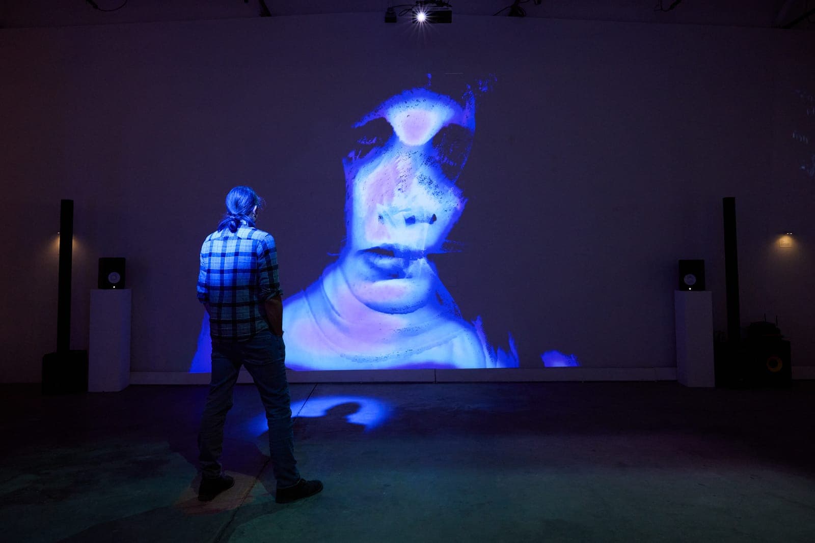 A visitor stands inside a projected portrait, their shadow folded into the face on the wall