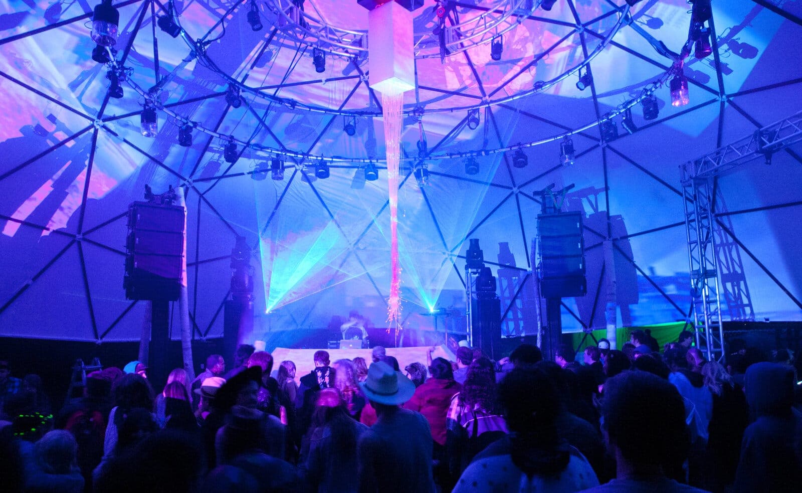 Inside a geodesic dome at night: projection-mapped visuals and stage lighting wash a festival crowd in violet and blue