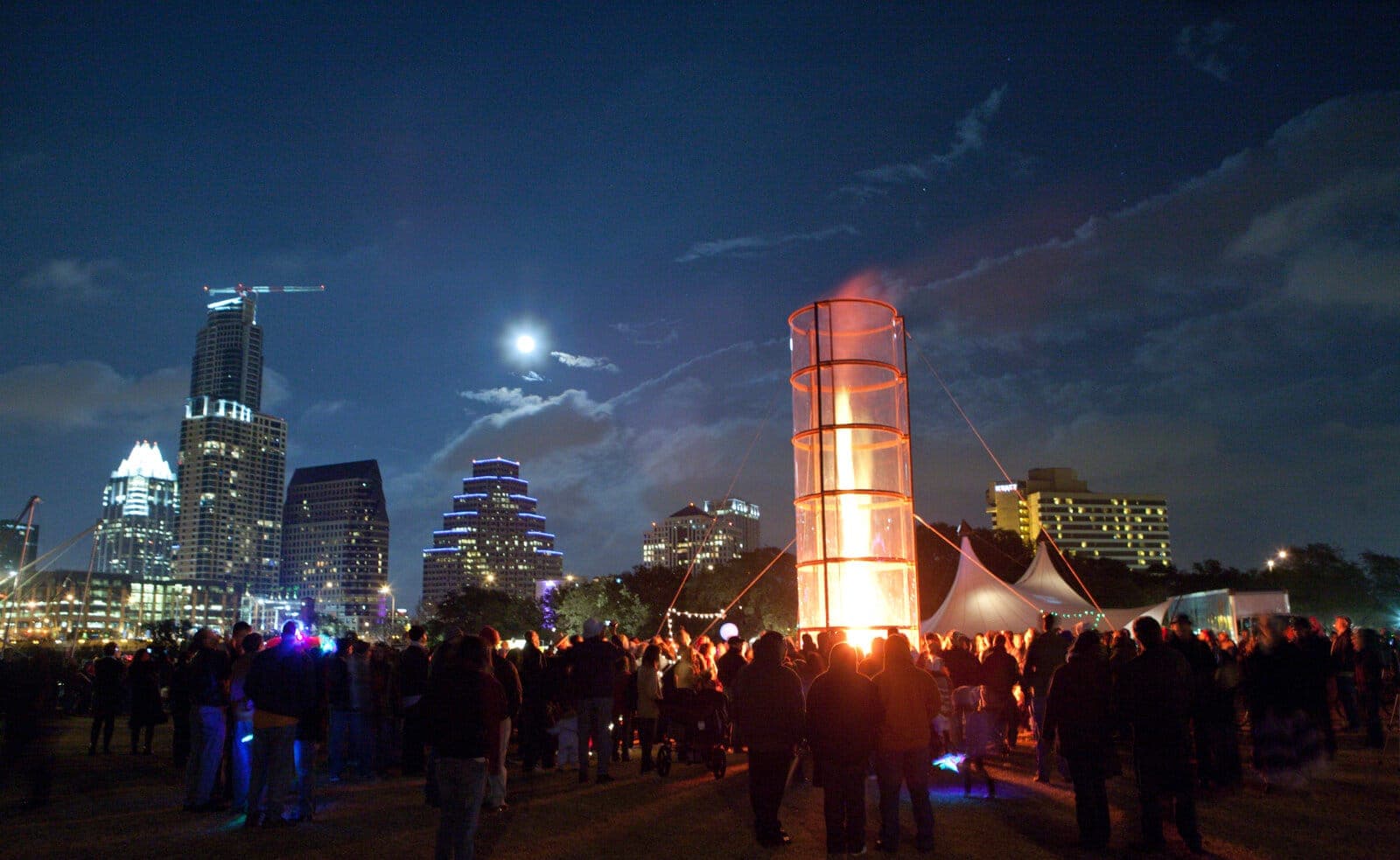 Fire tower installation glowing at night against the downtown Austin skyline, full moon overhead