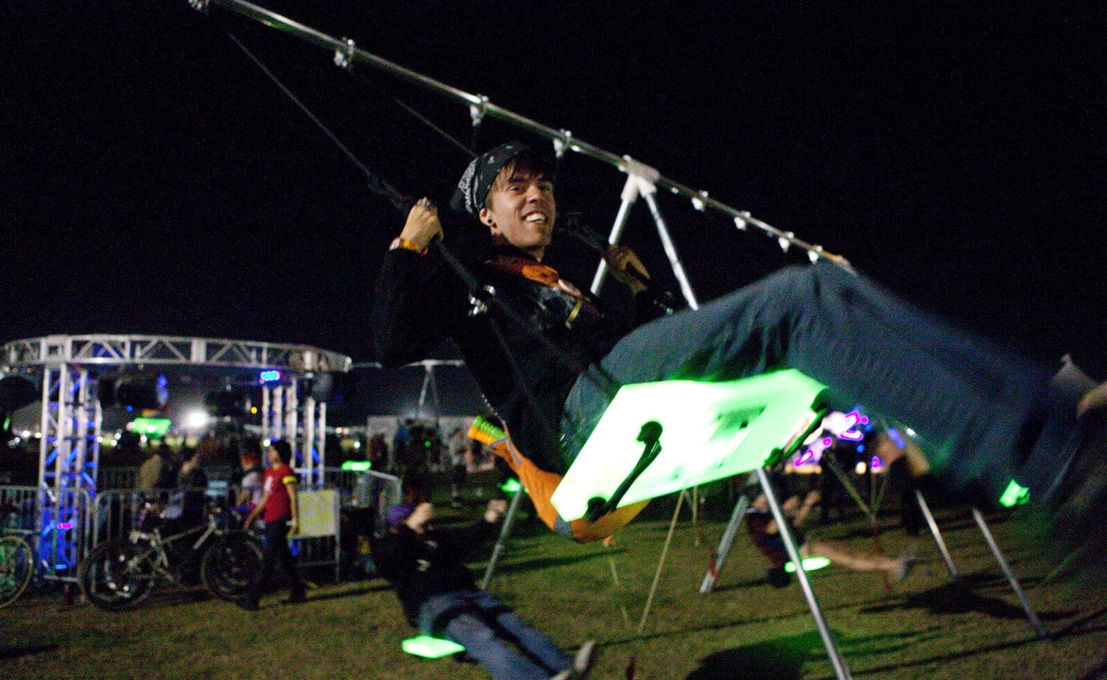 Rider mid-air on an LED-lit swing set at a nighttime festival