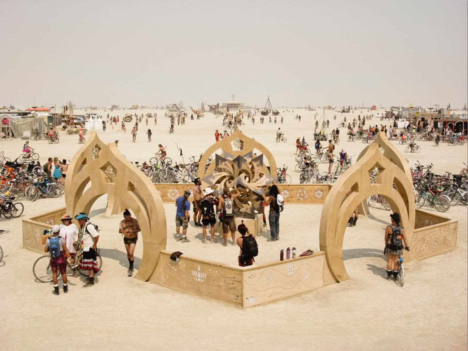 Daytime overview of the full café portal installation on the playa - arches, perimeter wall, and bikes streaming past