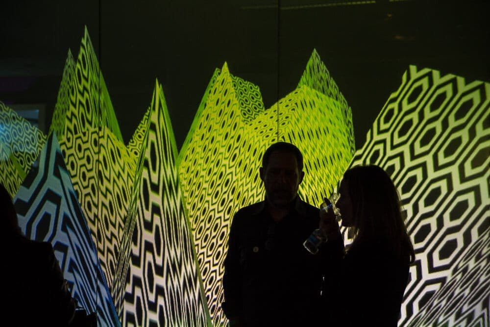 Silhouetted guests in conversation against jagged green-and-black generative pattern walls