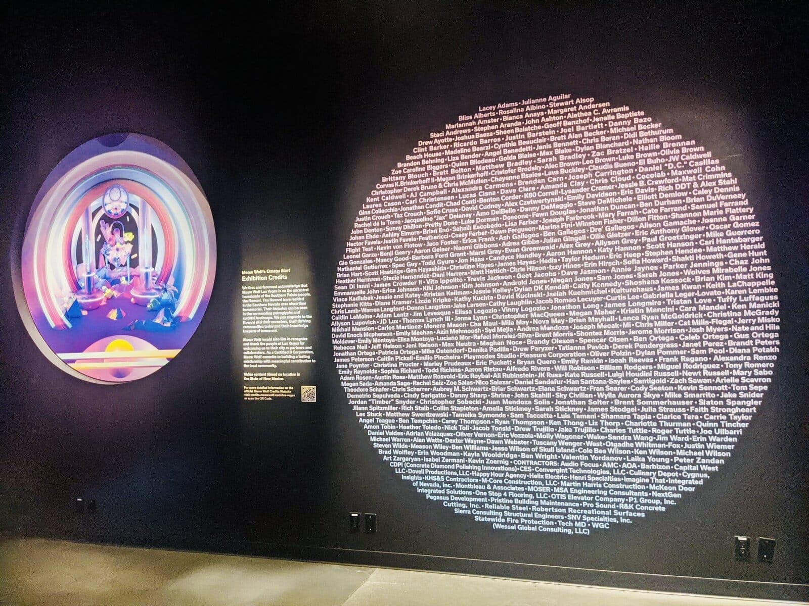 The Omega Mart exhibition credit wall at Meow Wolf Las Vegas: hundreds of contributor names set in a giant circle beside a portal view into the exhibit