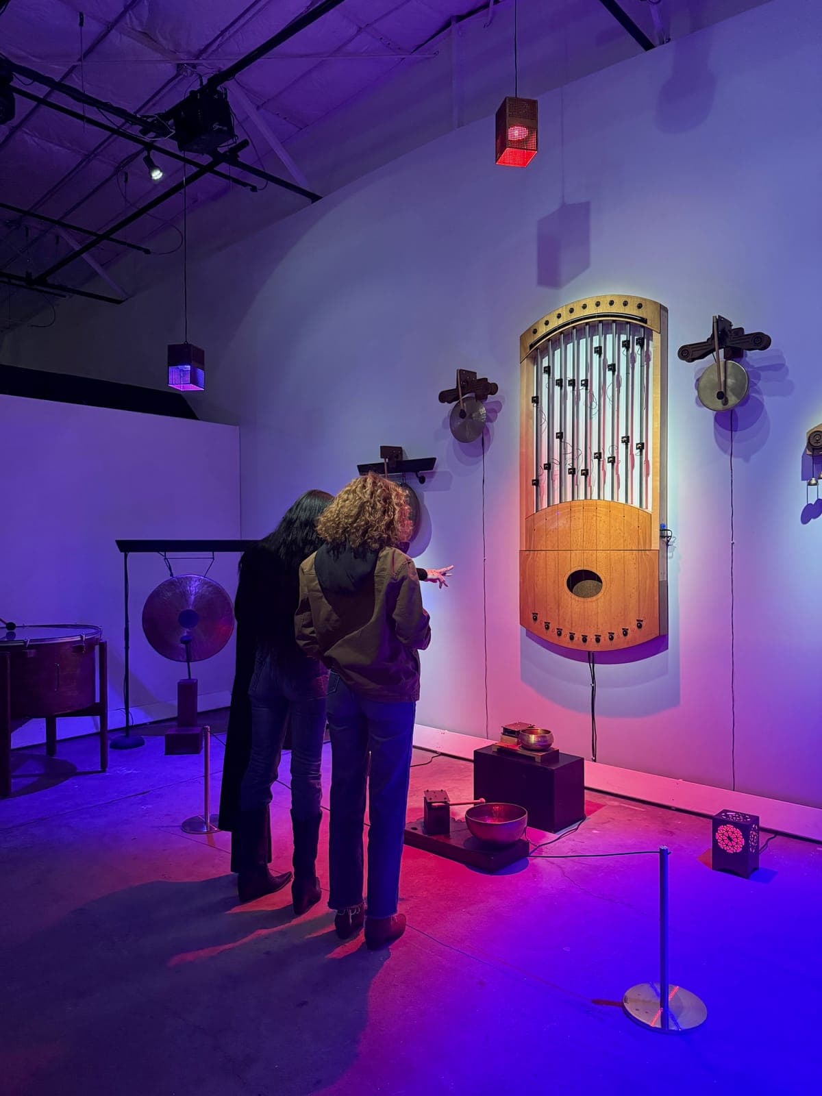 Visitors in violet light beside a wall-mounted mechanical pipe instrument and gong
