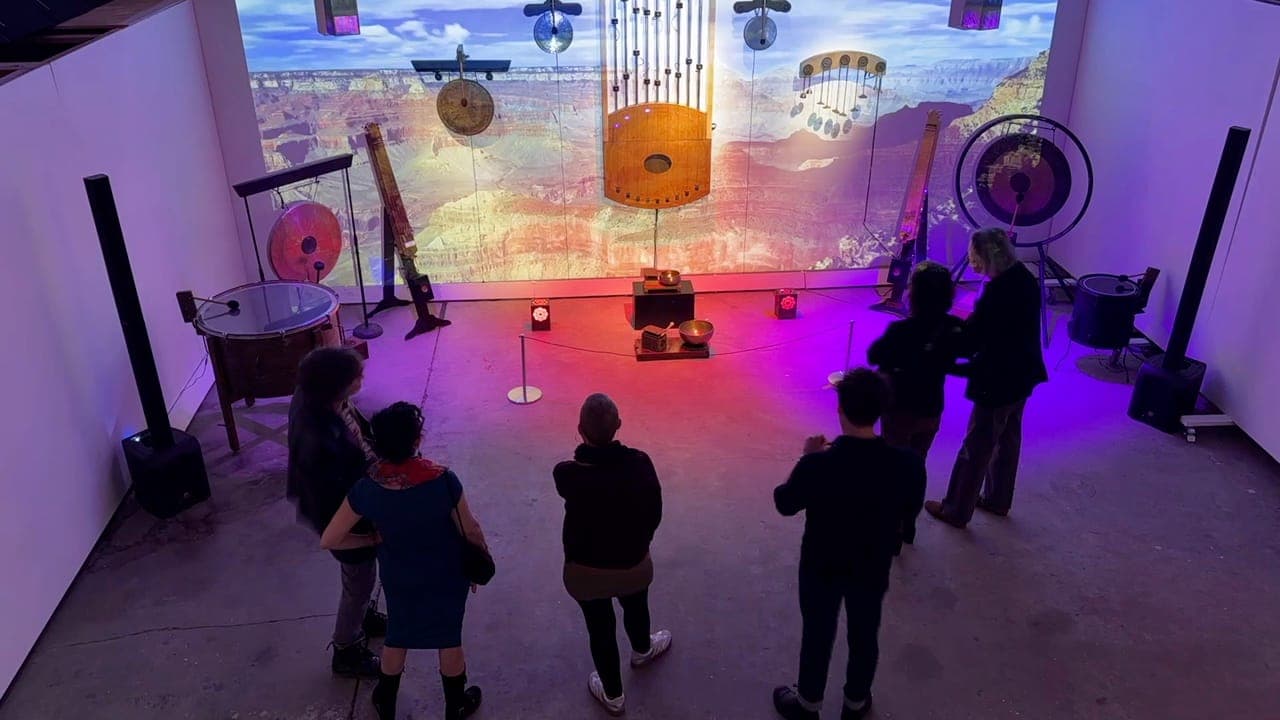 An audience seated before the Orchestrated Systems title wall during an artist talk