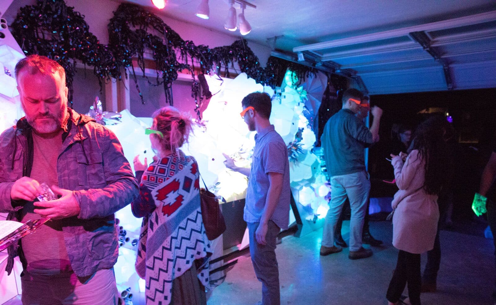 Visitors in colored glasses explore the glowing white barnacle wall inside the converted garage