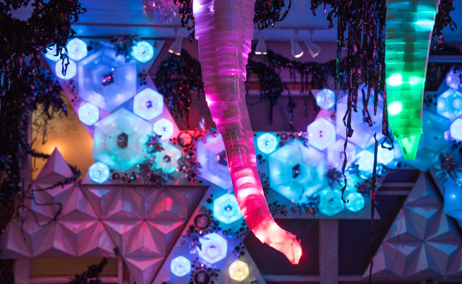 Glowing tentacle arcs over faceted white wall panels studded with hexagonal light cells