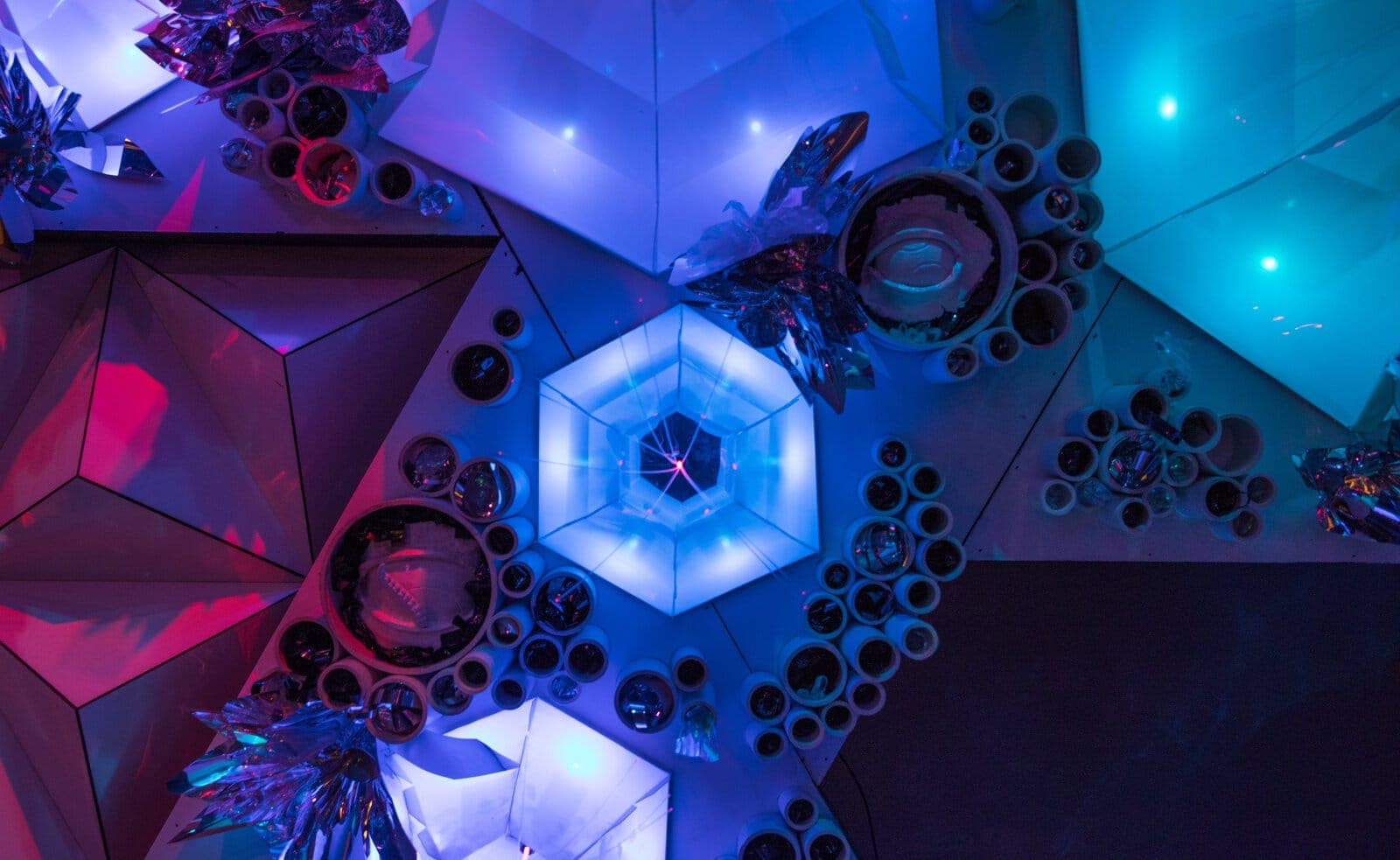 Wide view of the faceted barnacle wall in blue-violet light, hexagon portals glowing within